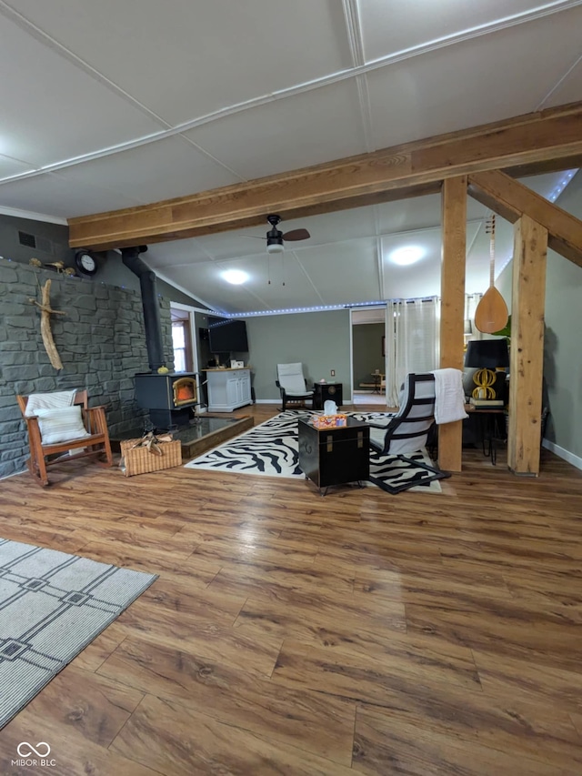 living room featuring vaulted ceiling with beams, hardwood / wood-style flooring, ceiling fan, and a wood stove