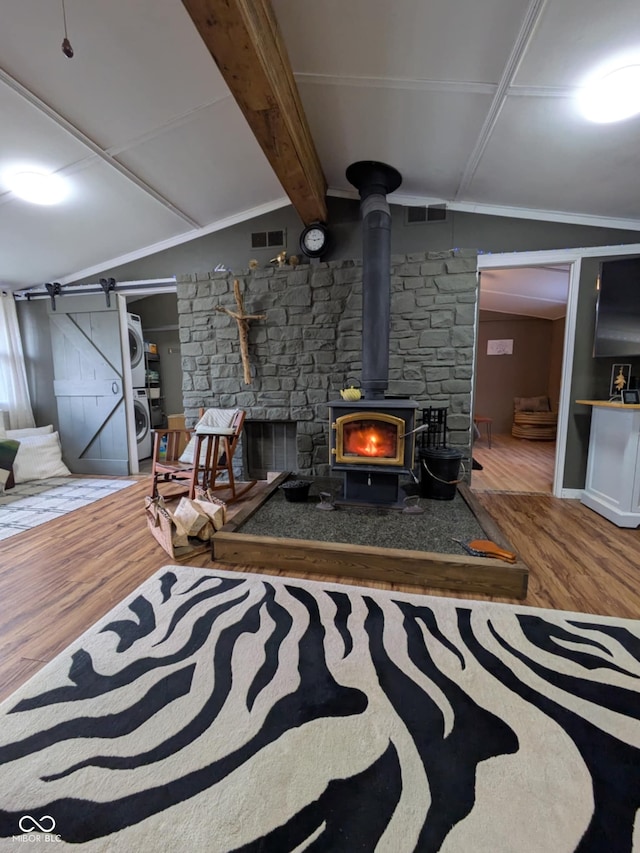 basement featuring wood-type flooring, a barn door, stacked washing maching and dryer, and a wood stove