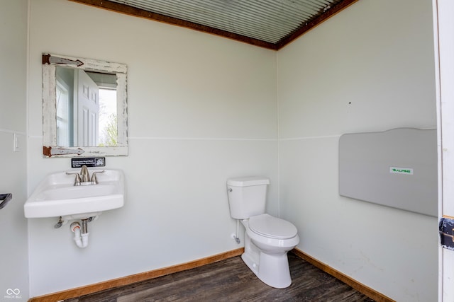 half bath with baseboards, a sink, toilet, and wood finished floors