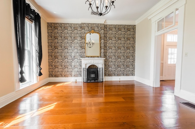 unfurnished living room with a chandelier, baseboards, ornamental molding, and a glass covered fireplace