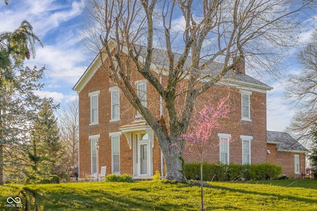 traditional-style house with a chimney, a front yard, and brick siding