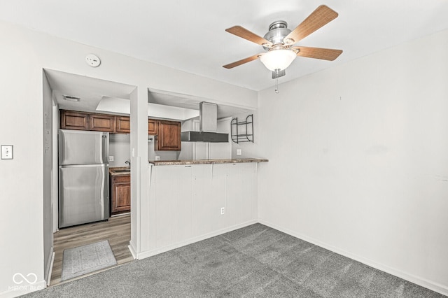 kitchen with light countertops, freestanding refrigerator, light carpet, a peninsula, and exhaust hood