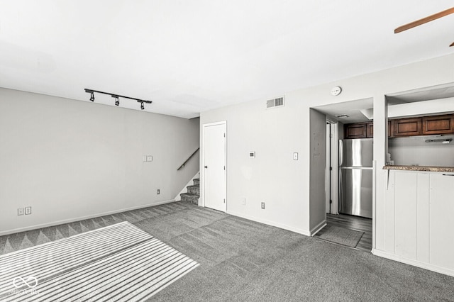 unfurnished living room featuring rail lighting, visible vents, carpet flooring, baseboards, and stairs