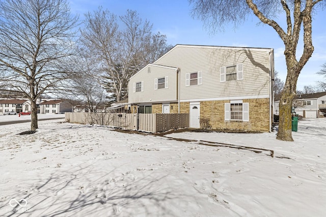 snow covered rear of property with fence and brick siding