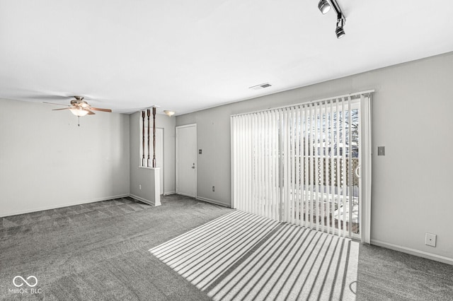 carpeted empty room featuring rail lighting, visible vents, ceiling fan, and baseboards