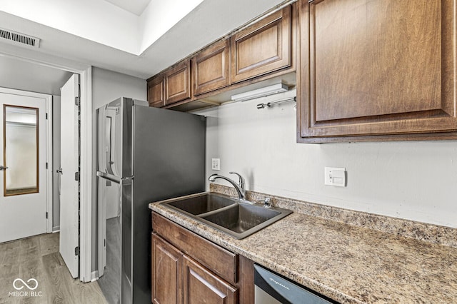 kitchen featuring light wood finished floors, stainless steel appliances, visible vents, a sink, and light stone countertops