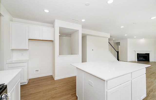 kitchen with white cabinetry, range, a center island, light wood-type flooring, and backsplash