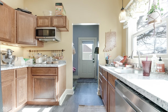 kitchen featuring light countertops, stainless steel appliances, a sink, light wood-type flooring, and pendant lighting