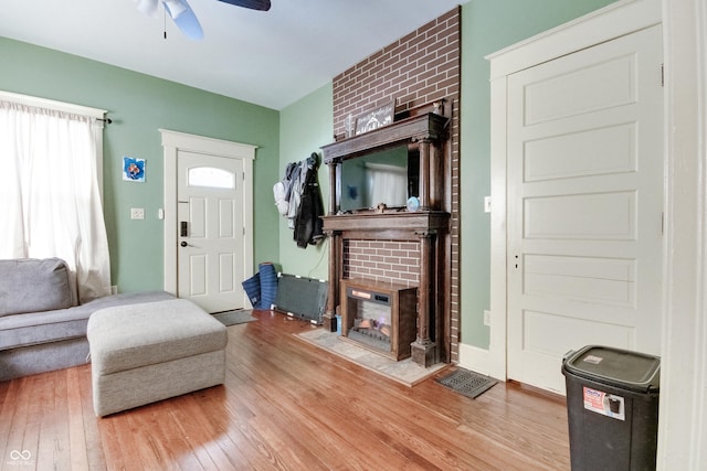 living area with ceiling fan, a brick fireplace, and wood finished floors