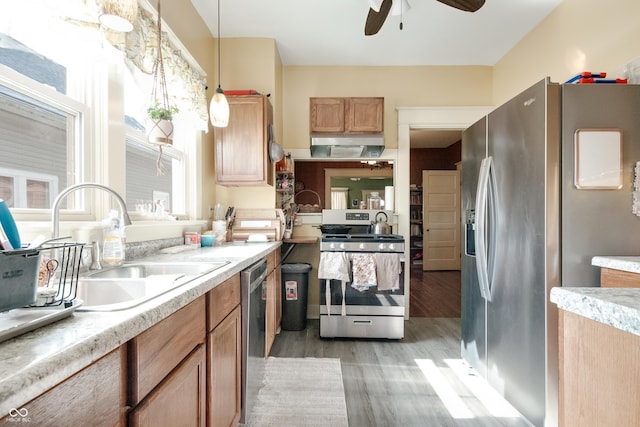 kitchen with a sink, pendant lighting, light countertops, light wood-type flooring, and stainless steel appliances