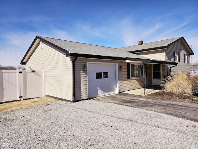 back of house featuring a garage, a shingled roof, a gate, and gravel driveway