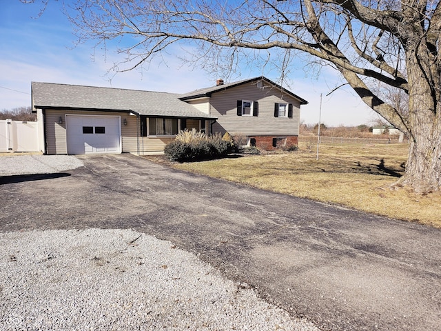 split level home with driveway, a shingled roof, a chimney, and an attached garage