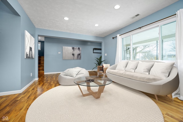 living area featuring recessed lighting, visible vents, a textured ceiling, wood finished floors, and baseboards