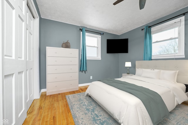 bedroom featuring a closet, a ceiling fan, a textured ceiling, wood finished floors, and baseboards