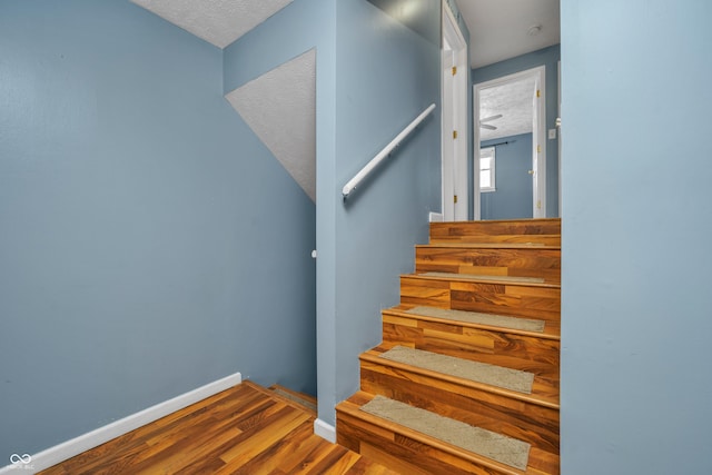 stairway with a textured ceiling, baseboards, and wood finished floors