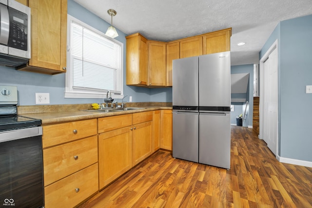 kitchen featuring appliances with stainless steel finishes, dark wood-type flooring, a sink, and pendant lighting