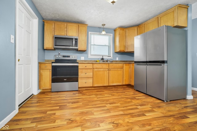 kitchen with light wood-style floors, appliances with stainless steel finishes, pendant lighting, and light countertops