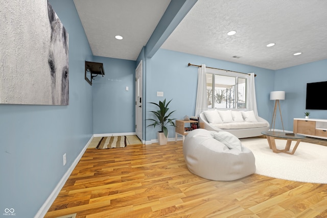 living area featuring light wood-style floors, baseboards, a textured ceiling, and recessed lighting