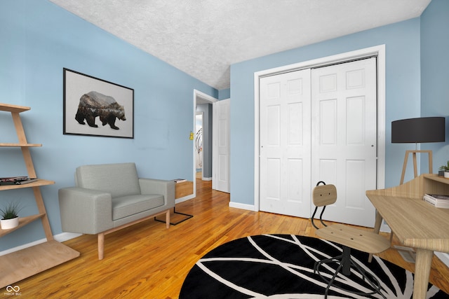 living area with a textured ceiling, baseboards, and light wood-style floors