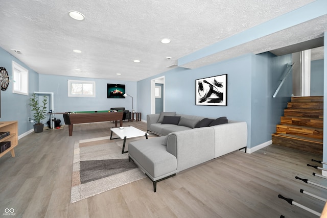 living area with light wood-style floors, stairway, a textured ceiling, and baseboards