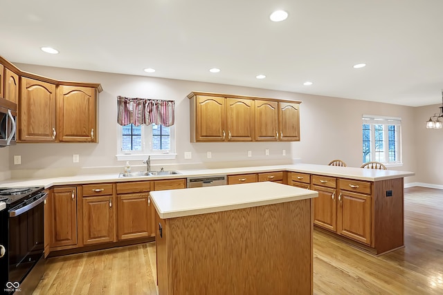 kitchen featuring decorative light fixtures, a peninsula, stainless steel appliances, light countertops, and a sink