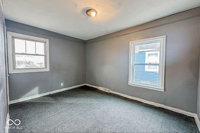 carpeted empty room featuring visible vents, baseboards, and a wealth of natural light