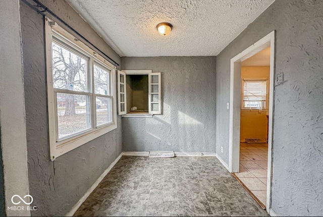 empty room featuring a textured wall, a textured ceiling, and baseboards