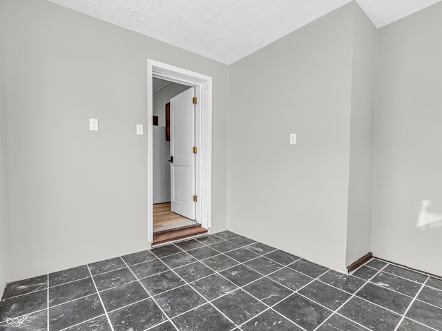 unfurnished room featuring a textured ceiling and dark tile patterned floors