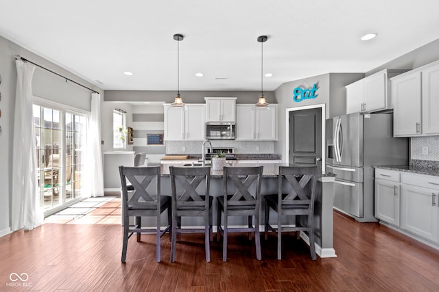 kitchen with white cabinets, an island with sink, dark wood-style flooring, and appliances with stainless steel finishes