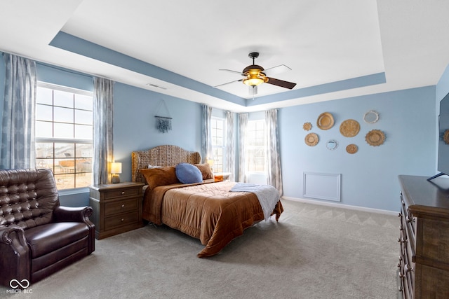 bedroom featuring a ceiling fan, baseboards, visible vents, a tray ceiling, and light colored carpet