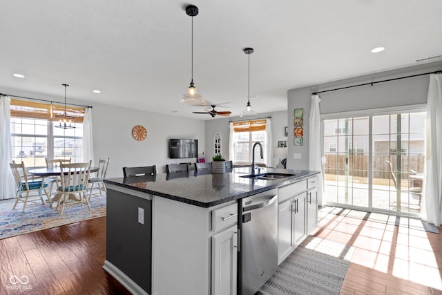 kitchen featuring an island with sink, hardwood / wood-style flooring, a sink, decorative light fixtures, and dishwasher