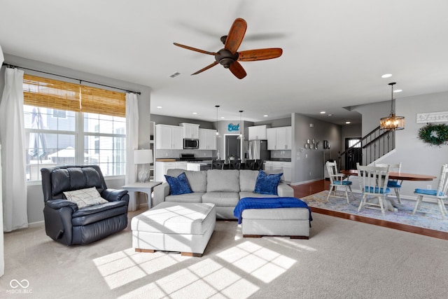 living room featuring visible vents, light carpet, ceiling fan with notable chandelier, recessed lighting, and stairs