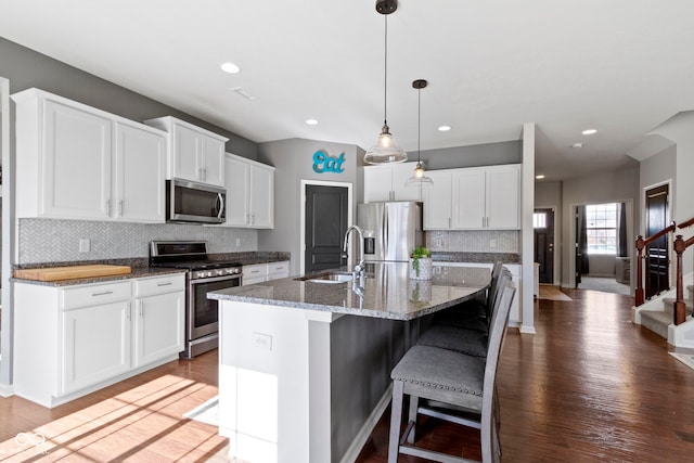 kitchen featuring a sink, appliances with stainless steel finishes, a kitchen breakfast bar, wood finished floors, and a kitchen island with sink