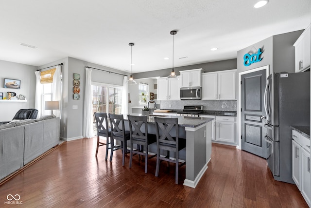 kitchen with tasteful backsplash, dark wood finished floors, open floor plan, a breakfast bar area, and stainless steel appliances