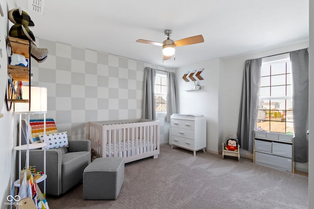 carpeted bedroom with visible vents, wallpapered walls, ceiling fan, a nursery area, and an accent wall