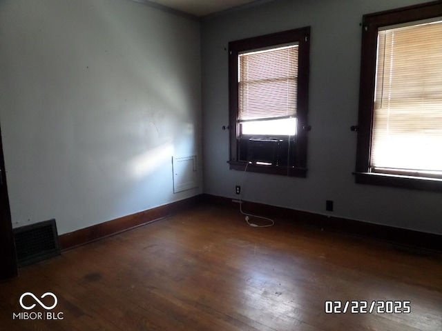 spare room with dark wood-style flooring, visible vents, and baseboards