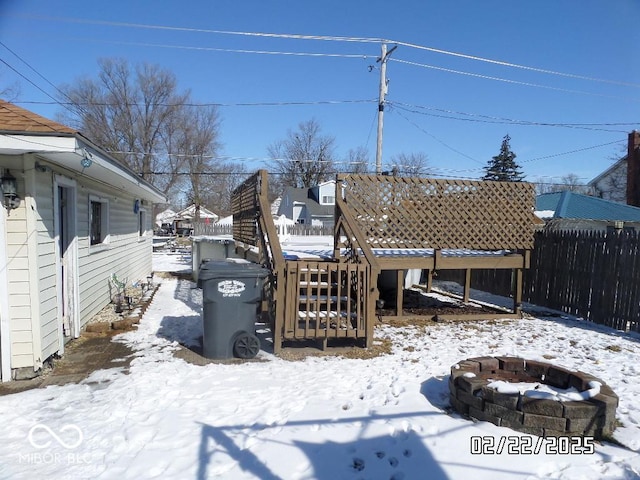 yard covered in snow with a deck, an outdoor fire pit, and fence