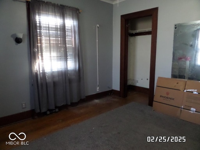 unfurnished bedroom featuring dark wood-type flooring, multiple windows, a closet, and baseboards