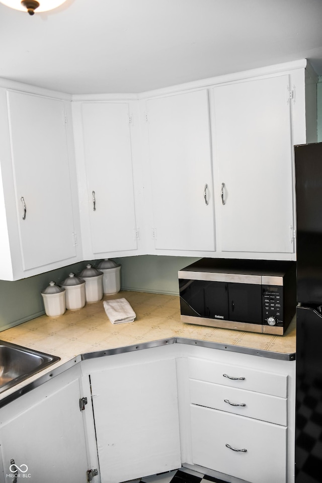 kitchen with black fridge, sink, and white cabinets