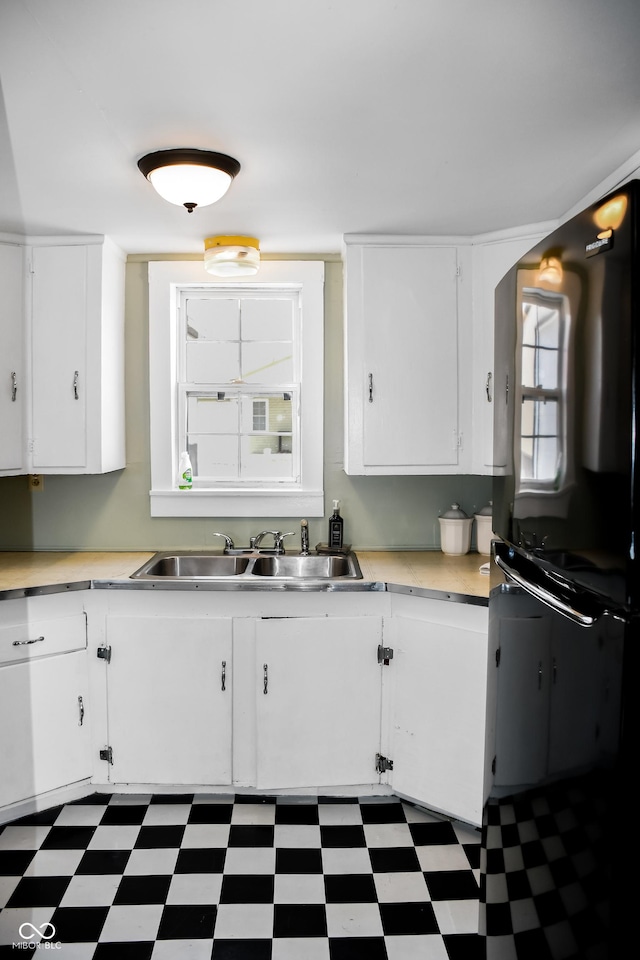 kitchen with white cabinetry, black refrigerator, and sink