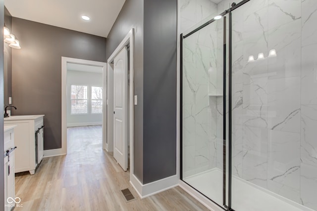 bathroom with baseboards, vanity, a marble finish shower, and wood finished floors