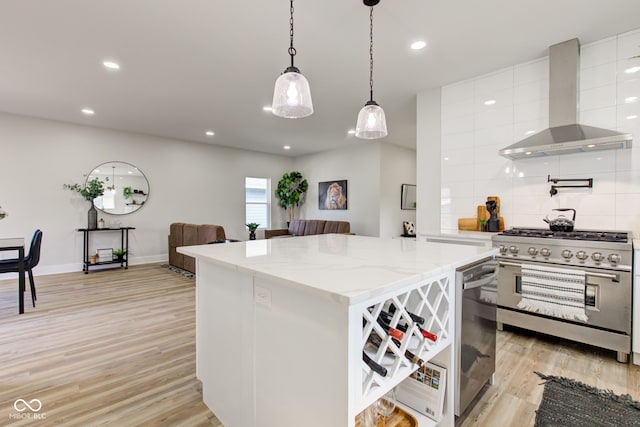 kitchen featuring a center island, light wood finished floors, stainless steel appliances, white cabinetry, and wall chimney range hood