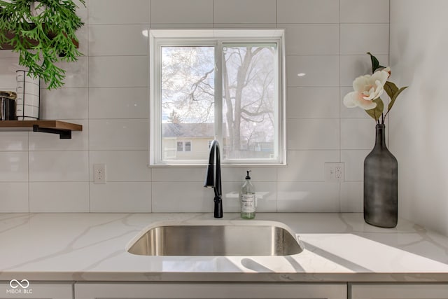 kitchen with tasteful backsplash, light stone counters, and a sink