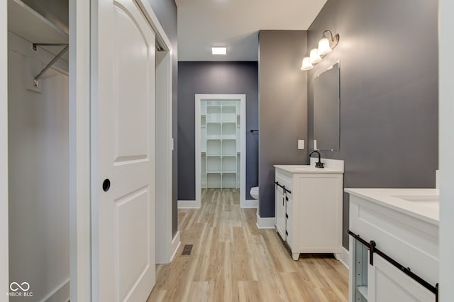 full bath with baseboards, visible vents, wood finished floors, a spacious closet, and two vanities