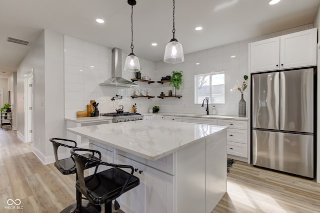 kitchen with tasteful backsplash, visible vents, freestanding refrigerator, a sink, and wall chimney exhaust hood