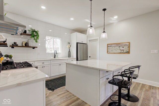 kitchen with light wood finished floors, a kitchen island, a breakfast bar, freestanding refrigerator, and a sink