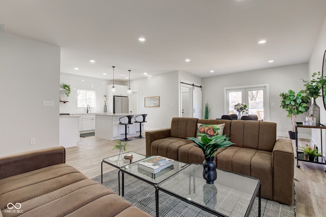 living room featuring light wood-type flooring, a barn door, baseboards, and recessed lighting