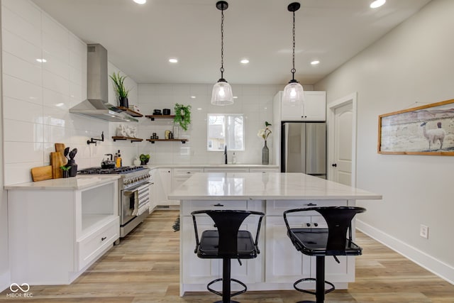 kitchen featuring light wood finished floors, decorative backsplash, wall chimney exhaust hood, appliances with stainless steel finishes, and open shelves