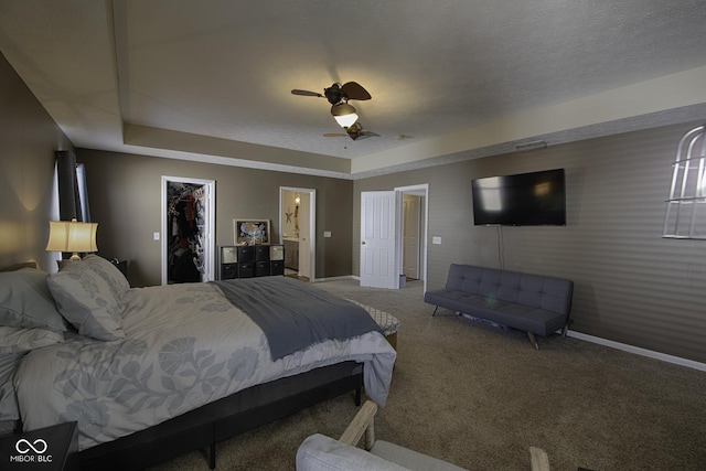 carpeted bedroom with a walk in closet, ceiling fan, a raised ceiling, a textured ceiling, and a closet