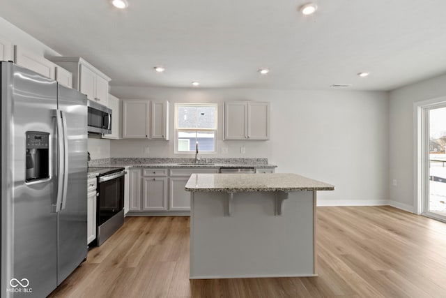 kitchen with light stone counters, a kitchen island, a sink, light wood-style floors, and appliances with stainless steel finishes